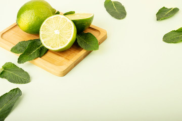 Fresh green limes on a pastel background. Mint leaves are laid out in the background and complement...