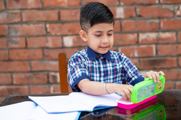 Cute little male student in school uniform writing on notebook while attending class in Primary school. He is using pencil box .