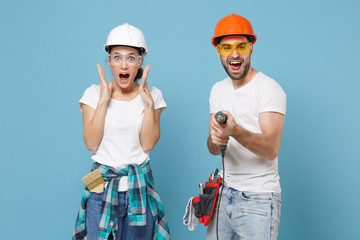 Shocked excited young couple woman man in protective helmet hardhat hold electric drill isolated on...