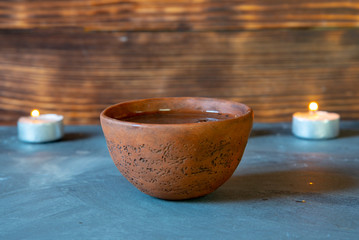 A ceramic bowl with tea and burning candles on a gray tabletop.