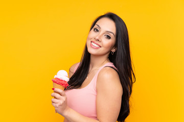 Young Colombian girl holding an cornet ice cream over isolated yellow background smiling a lot