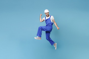 Naklejka na ściany i meble Happy young man in coveralls protective helmet hardhat isolated on blue background studio. Instruments accessories for renovation apartment room. Repair home concept. Jumping, doing winner gesture.
