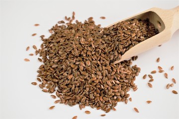 Flax seeds with a wooden scoop on a white background