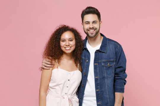 Smiling young couple two friends european guy african american girl in casual clothes posing isolated on pastel pink background. People lifestyle concept. Mock up copy space. Hugging, looking camera.