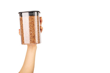 Buckwheat grains in a plastic container for storing cereals. Female hand holds a jar of buckwheat on a white isolated background. Buckwheat grains for proper nutrition.