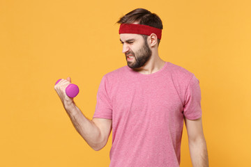 Tired young bearded fitness sporty guy sportsman in headband t-shirt spend weekend in home gym isolated on yellow background. Workout sport motivation concept. Doing exercise for arms with dumbbell.