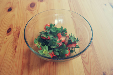 strawberry leaves from the green top part cut in a bowl - organic waste from cooking on a wooden table