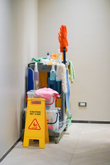 Caution Wet floor. Cleaning in progress. Wet floor sign with blurred cleaning trolley on the back.