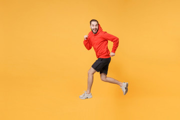 Fototapeta na wymiar Excited young bearded fitness sporty guy 20s sportsman in hoodie, shorts spend weekend in home gym isolated on yellow wall background. Workout sport motivation lifestyle concept. Jumping like running.