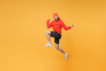 Fototapeta na wymiar Joyful young bearded fitness sporty guy 20s sportsman in hat hoodie shorts in home gym isolated on yellow background. Workout sport motivation lifestyle concept. Jump doing winner gesture screaming.