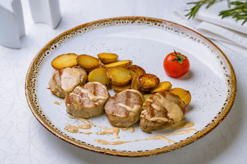 Pork medallions with baked mini potatoes on white plate