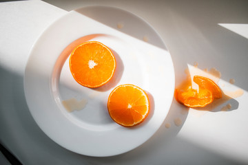 Two orange slices on a white plate with a hard light