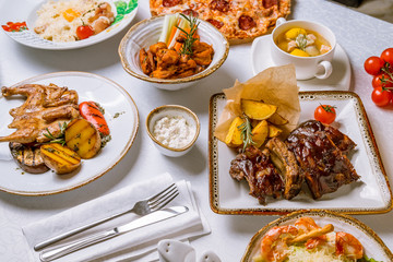 Assorted dishes on table. Barbecue pork ribs, chicken wings, pasta carbonara, pizza pepperoni, fish soup, chicken tabaka, steak file minion and caesar with shrimps.