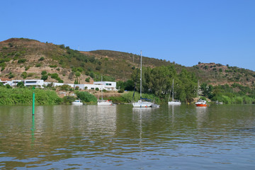 Fototapeta na wymiar Barcos fondeados en el río Guadiana en el tramo fronterizo entre España y Portugal. Al fondo se observa la orilla portuguesa perteneciente a la pequeña localidad de Alcoutim.
