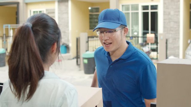 Young postal delivery courier man holding parcel boxes for sending to customer, Asian women signing and pay via qr code on mobile phone for receive delivered parcels outdoors.