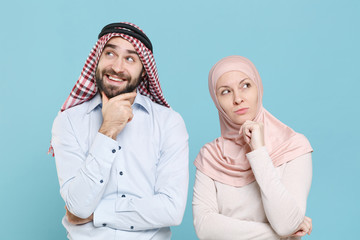 Pensive young couple friends arabian muslim man wonam in keffiyeh kafiya ring igal agal hijab clothes isolated on blue background studio. People religious lifestyle concept. Put hand prop up on chin.