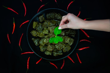 Traditional georgian dolma in grape leaves on black table with female hand