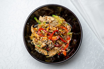 Rice noodles with chicken and vegetables on black plate