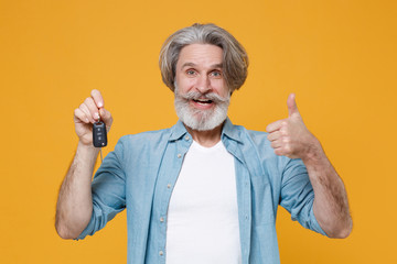 Funny elderly gray-haired mustache bearded man in casual blue shirt posing isolated on yellow wall background studio. People lifestyle concept. Mock up copy space. Hold car keys, showing thumb up.