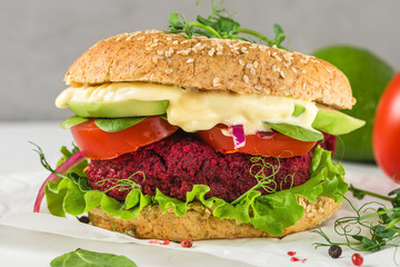 Vegan beetroot burger with avocado, salad, tomato, sprouts and vegan mayonnaise on white marble table