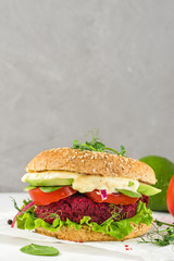 Vegan beetroot burger with avocado, salad, tomato, sprouts and vegan mayonnaise on white marble table. vertical orientation