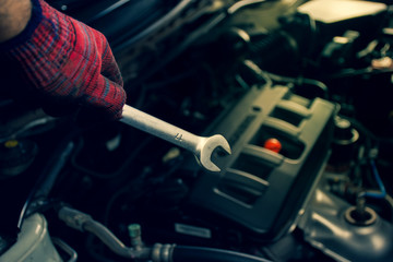 Hand of mechanic professional man hold a wrench tools with car engine blurred background,Automotive maintenance concept.