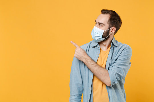 Young man in sterile face mask posing isolated on yellow background studio portrait. Epidemic pandemic spreading coronavirus 2019-ncov sars covid-19 flu virus concept. Pointing index finger aside up.