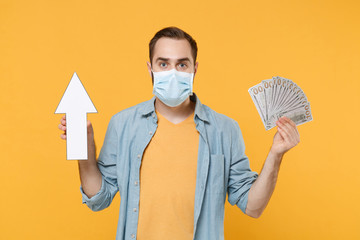 Young man in sterile face mask posing isolated on yellow wall background. Epidemic pandemic...