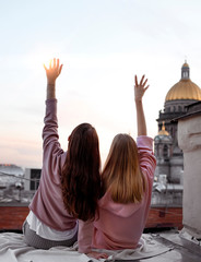 Two girls are sitting back view on the roof