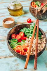 Vegan Buddha bowl. Healthy meal quinoa, tomato, cucumber, carrot, radish, corn salad in coconut bowls on blue rustic background.