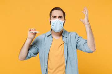 Angry young man in sterile face mask posing isolated on yellow background in studio. Epidemic...