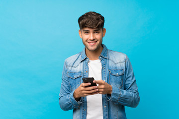 Young handsome man over isolated blue background sending a message or email with the mobile