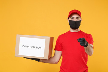 Delivery man employee in red cap blank t-shirt uniform face mask glove hold donations cardboard box isolated on yellow background studio Service quarantine pandemic coronavirus virus 2019-ncov concept