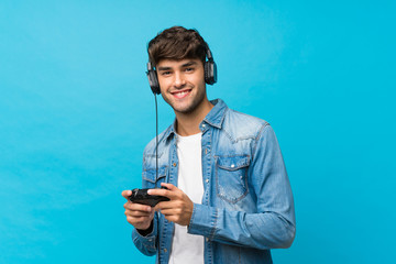 Young handsome man over isolated blue background playing at videogames