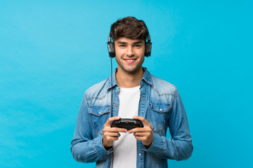 Young handsome man over isolated blue background playing at videogames