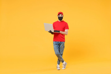 Delivery man in red cap blank t-shirt uniform mask gloves isolated on yellow background studio Guy employee work hold laptop pc computer Service quarantine pandemic coronavirus virus 2019-ncov concept