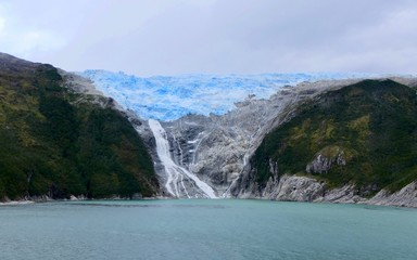 Glacier with waterfall in chilean fjord, blue ice and clouds, glacier alley, Beagle Channel