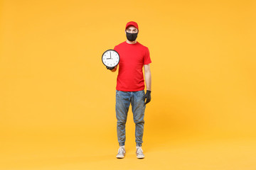 Delivery man in red cap blank t-shirt uniform sterile face mask gloves isolated on yellow background studio Guy employee working courier hold clock Service pandemic coronavirus virus 2019-ncov concept
