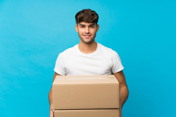 Young handsome man over isolated blue background holding a box to move it to another site