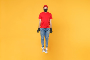 Naklejka premium Fun jumping delivery man in red cap t-shirt uniform sterile face mask gloves isolated on yellow background studio Guy employee courier Service quarantine pandemic coronavirus virus 2019-ncov concept.