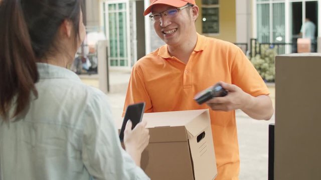 Young postal delivery courier man holding parcel boxes for sending to customer, Asian women signing and pay via qr code on mobile phone for receive delivered parcels outdoors. 4k Slow motion.