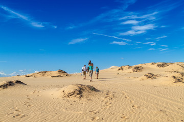 Three people walk in the desert, view from the back