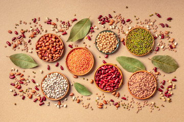 Legumes assortment, shot from the top on a brown background. Lentils, soybeans, chickpeas, red...