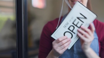 Small business owner smiling while turning the sign for the reopening of the place after the quarantine due to covid-19. Happy businesswoman turn the sign from closed to open sign. - Powered by Adobe