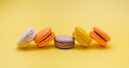 A set of macarons on a yellow background. macarons is yellow, orange, cream, brown. Five macarons are stacked in a row. Сopy space.