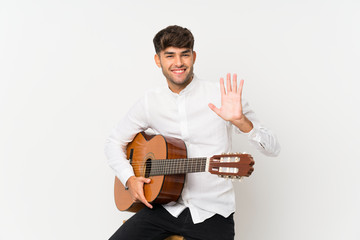 Young handsome man with guitar over isolated white background saluting with hand with happy expression