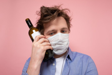 Sad caucasian man in medical mask complaining and drinking wine alone.