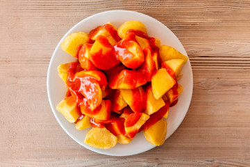 Patatas bravas, typical Spanish food. Potato with a spicy sauce, shot from the top on a wooden table