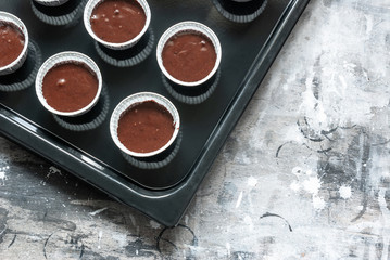 Chocolate dough for muffins in paper molds on a black baking sheet. Cozy culinary cover, concept, cooking at home.