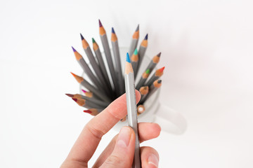 One green pensil on the hand. A colorful pencils in a glass in the white background. Drawing by pencils. Hobby during quarantine. 